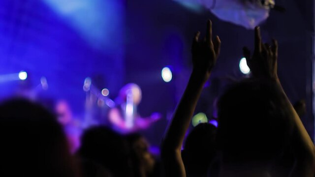 People crowd partying, raising hands up, showing sign - devil horns gesture at rock concert in front of stage of nightclub. Colorful stage lighting. Nightlife and entertainment concept
