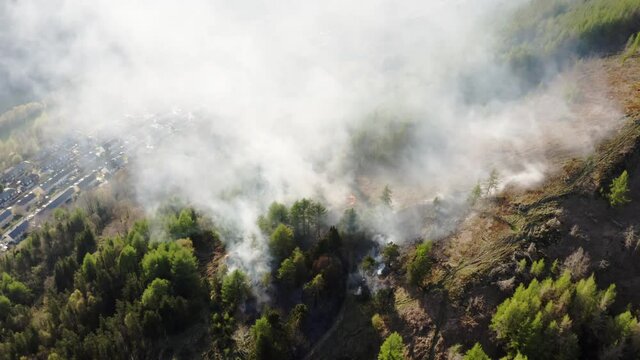 Aieral view of fire spreading on a mountain forest bank from kids starting fires in forest area. south wales uk