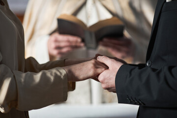 Close-up of young couple holding hands and getting married in the church