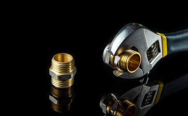 Plumbing brass fittings and adjustable spanner closeup on black background during repair or...