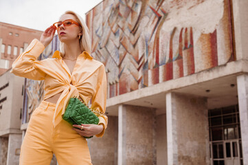 Street style, summer fashion portrait of happy smiling fashionable woman wearing  total orange outfit: sunglasses, shirt, jeans, holding trendy quilted green leather bag. Copy, empty space for text