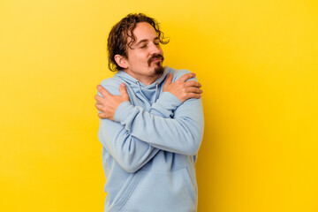 Young caucasian man isolated on yellow background hugs, smiling carefree and happy.
