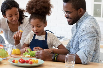 Happy family couple and daughter girl preparing salad in kitchen for keeping healthy eating...