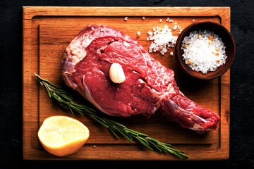 Raw beef steak on a wooden cutting board on black background - 430248648