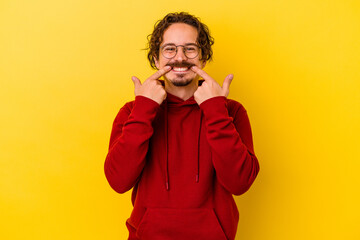 Young caucasian man isolated on yellow background smiles, pointing fingers at mouth.