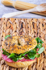 Freshly made and baked bagel with salami and lamb's lettuce (Valerianella locusta). Pastry and home cooking concept. Vertical photo and selective focus