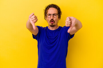 Young caucasian man isolated on yellow background showing thumb down and expressing dislike.