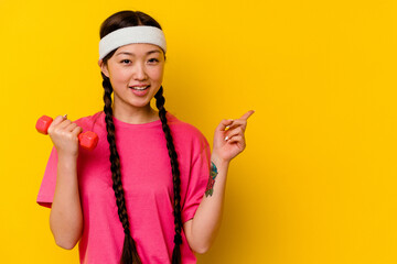 Fototapeta na wymiar Young sport chinese woman isolated on yellow background smiling and pointing aside, showing something at blank space.