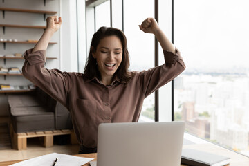 Overjoyed young Caucasian female employee look at laptop screen triumph reading good news online....