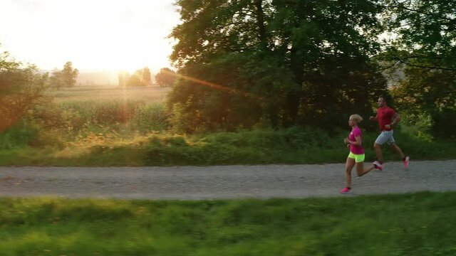 Tracking shot of a Caucasian couple in sportswear running along a dirt road near cornfields