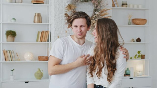 Young caucasian couple married man and woman millennials standing together embracing posing, funny guy boyfriend blow puffing out cheeks holding breath girl girlfriend laughing sincerely loudly smile