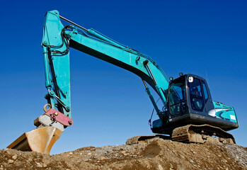 Blue excavator on mud hill with blue sky