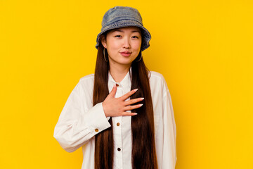 Young chinese woman isolated on yellow background taking an oath, putting hand on chest.