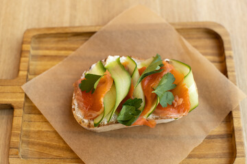 Appetizing bruschetta sandwich made from whole grain bread, with red fish and curd cheese, with thinly sliced ​​cucumber. Concept of healthy food, healthy snacks. Top view, soft selective focus