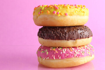 three Berliners donut pink yellow chocolate with a sprinkle on a pink background leit stack on top of each other with a place for text and with a copyspace