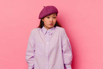 Young chinese woman isolated on pink background shrugs shoulders and open eyes confused.