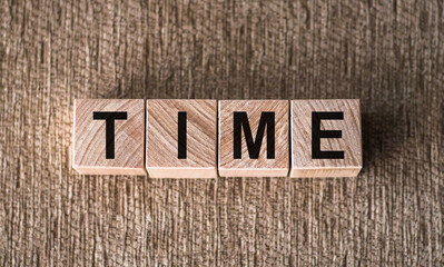TIME - word written on wooden blocks on a brown background.