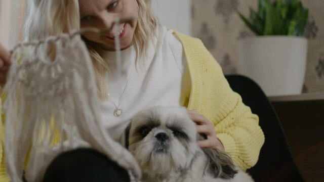 Woman weave macrame decoration with dog at home. Rbbro female stroking pet and make craft of rope