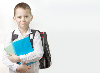 Schoolboy with a backpack and books in hands on a light background