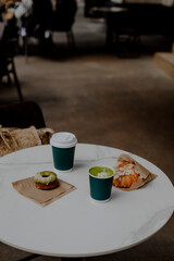 two cups of hot drinks to go. matcha latte to go. two paper cups with a drink on a white table in a...