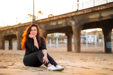 A modern young woman sits on the sand in Manhattan Beach in the early morning