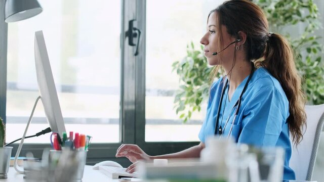 Video of beautiful female doctor working and typing with computer at consultation.