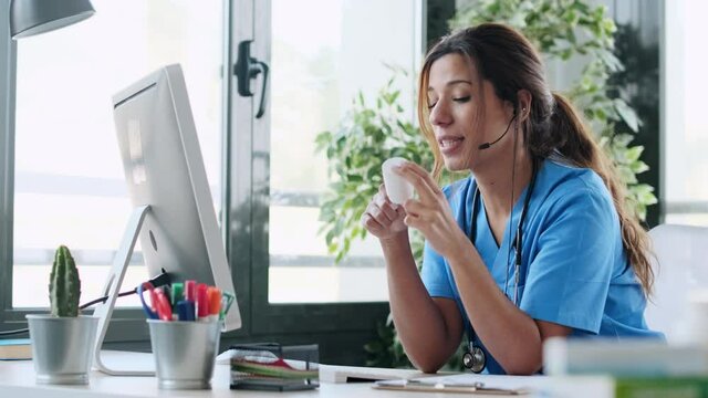 Video of beautiful female doctor talking with earphone while explaining medical treatment to patient through a video call with computer in the consultation.