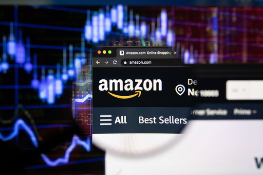 Amazon company logo on a website with blurry stock market developments in the background, seen on a computer screen through a magnifying glass