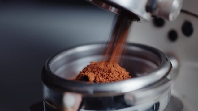 Professional barista worker use grinder machine to grind fresh coffee beans for make hot beverage at coffee cafe shop. Extreme macro close up