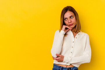 Young caucasian skinny woman isolated on yellow background looking sideways with doubtful and skeptical expression.