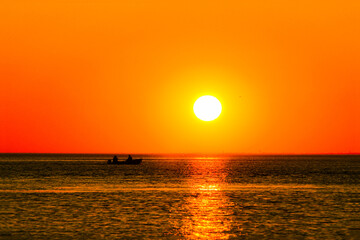 setting sun over the sea with reflection in the water and a sailing boat