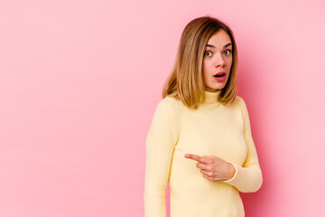 Young caucasian woman isolated on pink background smiling and pointing aside, showing something at blank space.