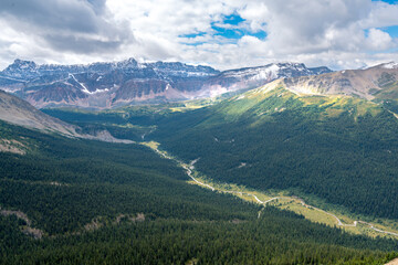 Clouds gathering above mighty rock massive of Evelyn Peak and green valley bellow. Cloudy summer day in Canadian Rockies. Bald Hills trail in Jasper National Park, Canada.