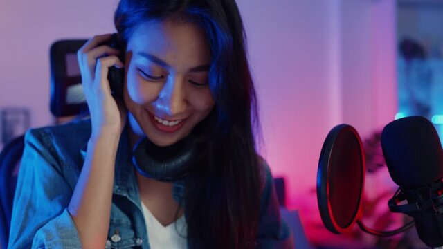 Happy asia girl dj play launchpad synthesizer keyboard sound mixer wear headphone and performance music online live talk with audience in living room home studio at night. Content creator concept.