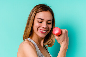 Young sport skinny caucasian holding a dumbbell woman isolated on blue background