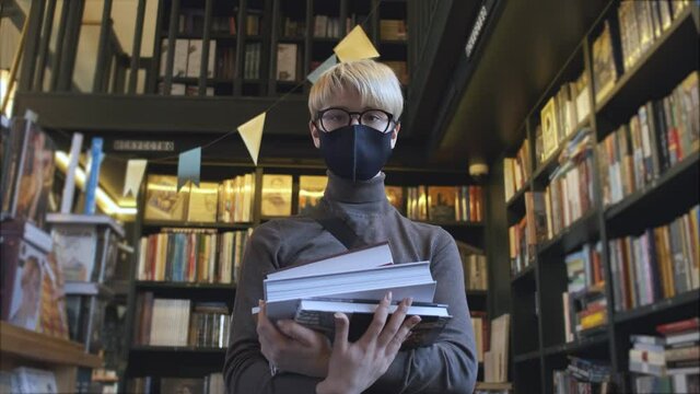 portrait of androgyne in protective mask holding a stack of books in the library