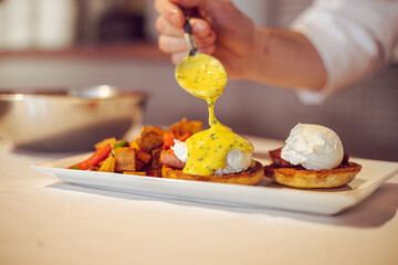 chef preparing eggs benedict with hollandaise sauce in a kitchen at a fine dining restaurant during...