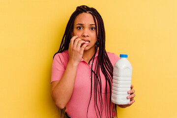 Young african american woman holding a milk bottle isolated on yellow background biting fingernails, nervous and very anxious.