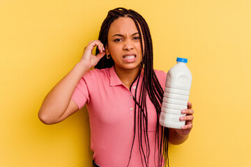 Young african american woman holding a milk bottle isolated on yellow background covering ears with hands.