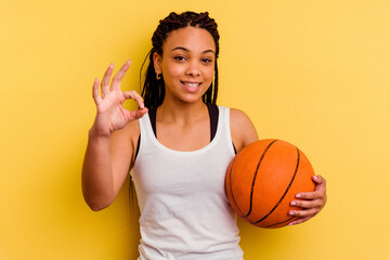 Young african american woman playing basketball isolated on yellow background cheerful and...