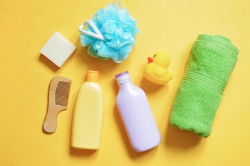 Shampoo, shower gel, rolled green towel, com, soap and rubber duck. Baby care bath products on a yellow background
