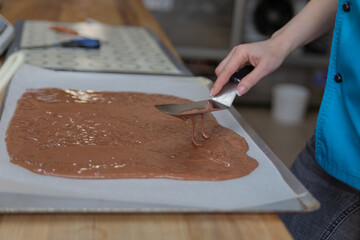 confectioner with a pastry spatula stretches chocolate dough on baking paper