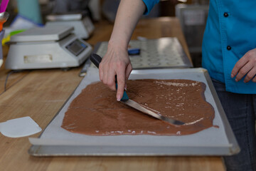 confectioner with a pastry spatula stretches chocolate dough on baking paper