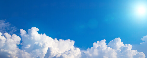 Blue sky background with white puffy clouds on a bottom foreground. Wide shot with cumulus clouds and cold blue sun. Banner, copy space, blank space for text - obrazy, fototapety, plakaty