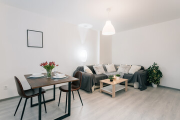 Living room connected with dining area. The interior is decorated in gray. The room is dominated by wooden materials and modern workmanship. Plants predominate among the decorative elements.