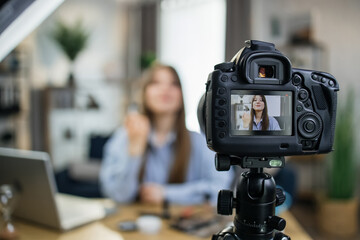 Charming caucasian woman using modern camera for filming online tutorial about new cosmetics. Young...