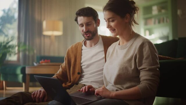 Couple Use Laptop Computer, while Sitting on the Living Floor room of their Apartment. Boyfriend and Girlfriend Talk, Shop on Internet, Choose Product to Order Online, Doing Remote Work Together - Powered by Adobe