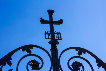 Forged gate with a cross at the entrance to the cathedral against the blue sky. Forged date 1904.