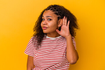 Young african american woman isolated on yellow background trying to listening a gossip.