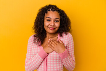 Young african american woman isolated on yellow background laughing keeping hands on heart, concept of happiness.